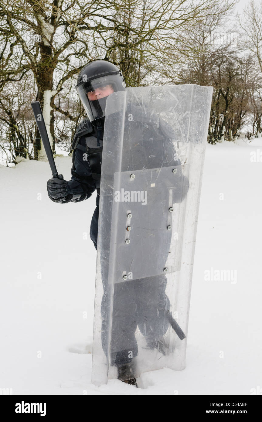 Police officer dressed in riot gear with shield in snow Stock Photo