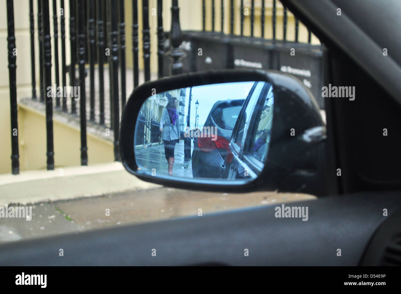 Wing mirror of car featuring woman walking towards it with head turned away Stock Photo