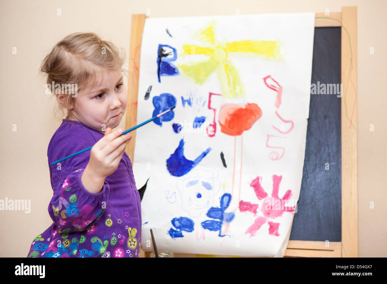 Cute Caucasian girl standing with painting brush near easel Stock Photo ...