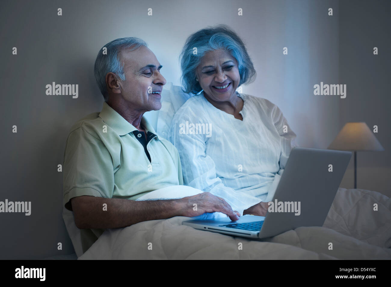 Couple using a laptop on the bed and smiling Stock Photo - Alamy