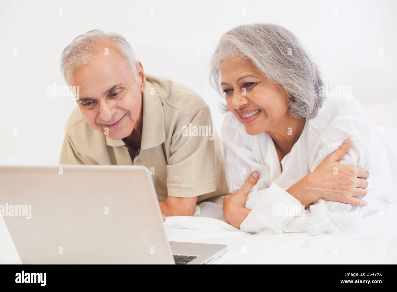 Couple using a laptop on the bed and smiling Stock Photo - Alamy