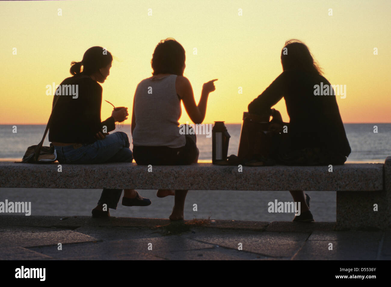 Young women sipping mate drink from gourds at sunset in Montevideo, Uruguay Stock Photo