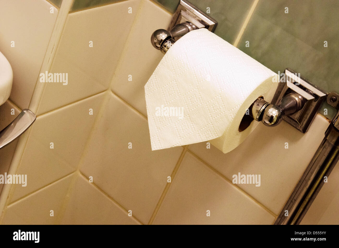 Folded end of toilet roll on a chrome holder in a tiled hotel bathroom. Stock Photo