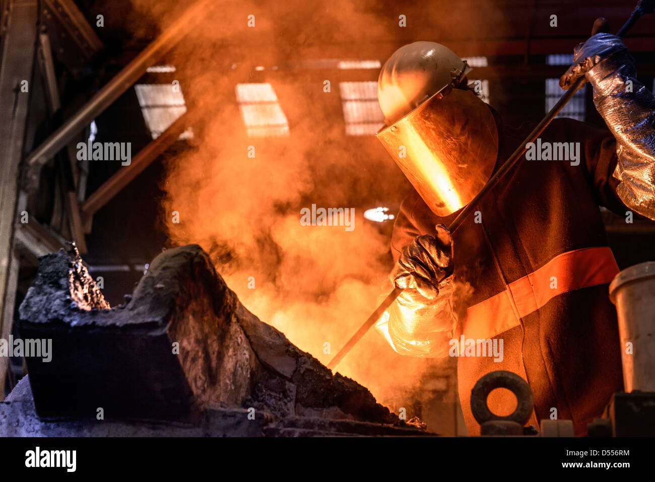 Worker stirring molten metal in foundry Stock Photo