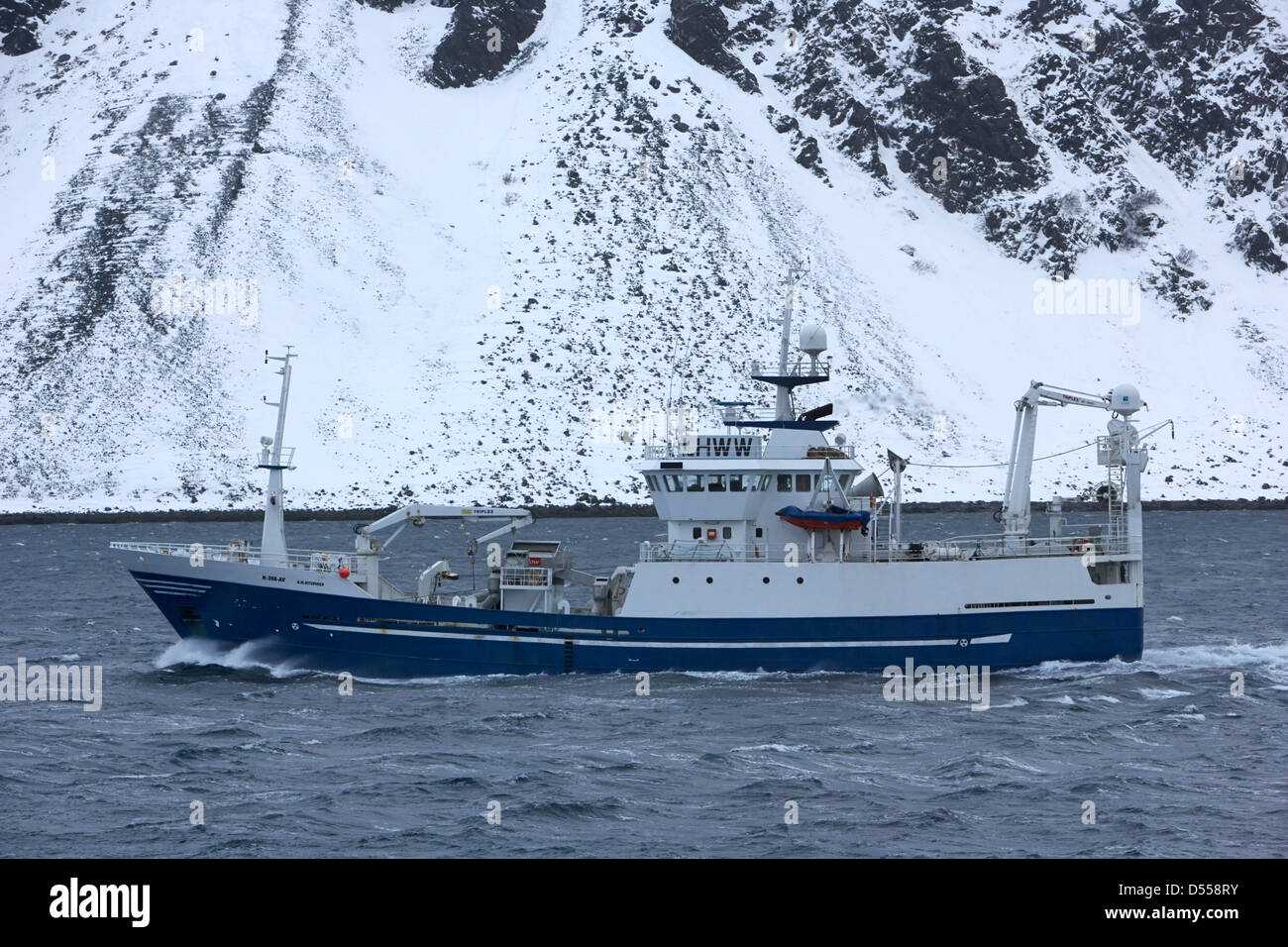 km ostervold purse seiner pelagic trawler sailing past snow covered fjord coastline norway europe Stock Photo