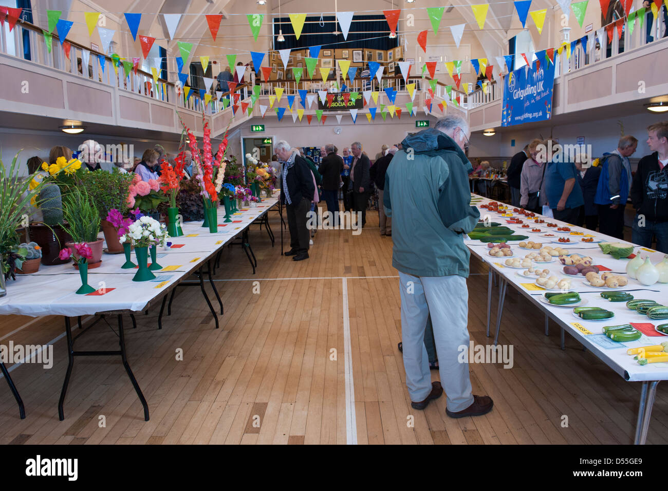 People view bright flowers & fresh veg produce displayed on tables in