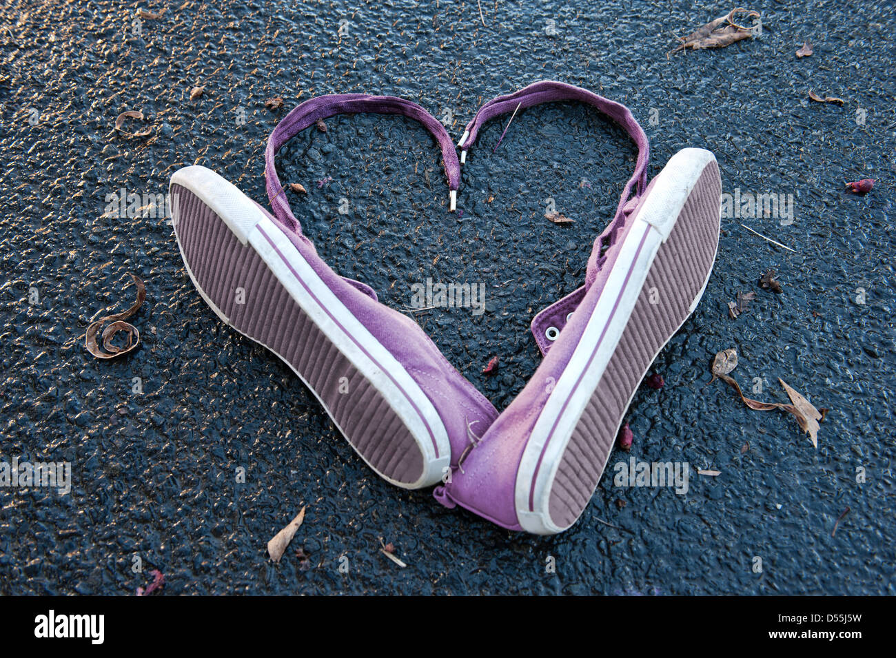 Purple Sneakers arranged in the shape of a heart on a wet tar road with some winter leaves. Stock Photo