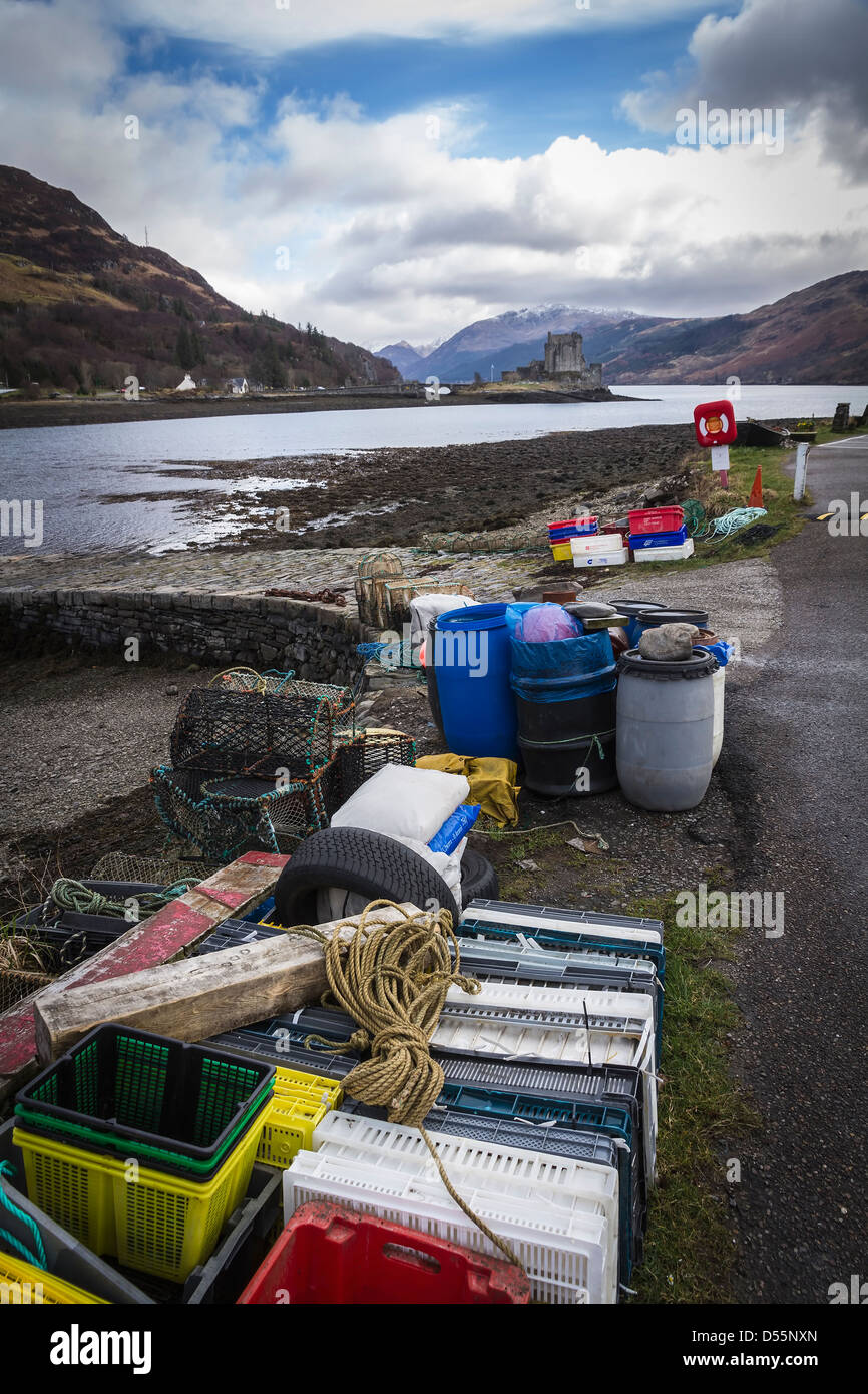 Brightly coloured plastic fish containers and lobster pots on the shore of Loch Duich, Eilean Donan Castle in the background. Stock Photo