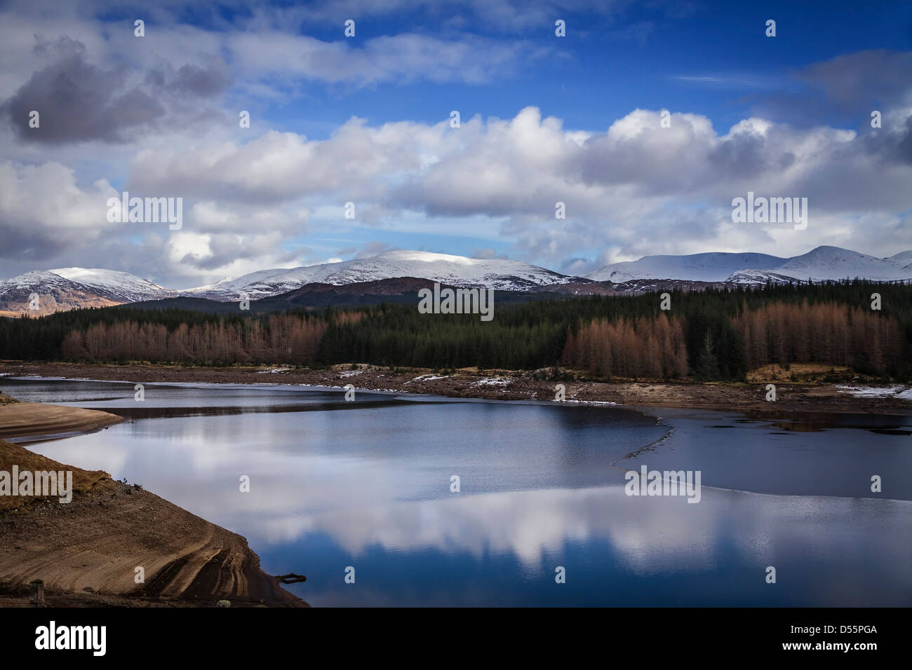 Low water on a partially frozen Loch Laggan with snow covered mountains in the background, Western Highlands, Scotland Stock Photo