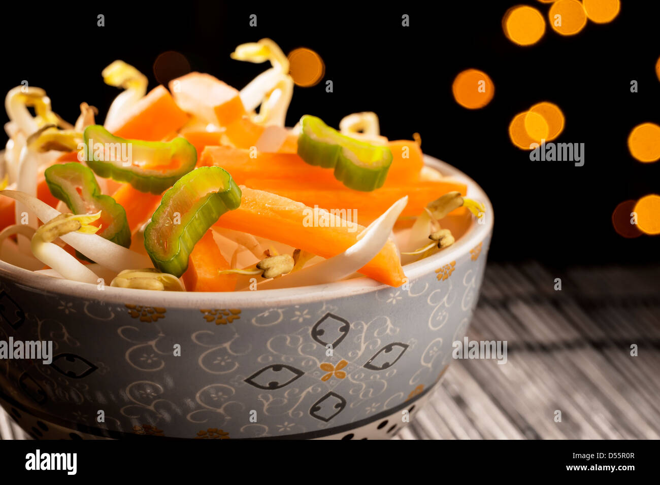 Closeup of a bowl with Asian vegetables on black bamboo mat and lights in the background Stock Photo