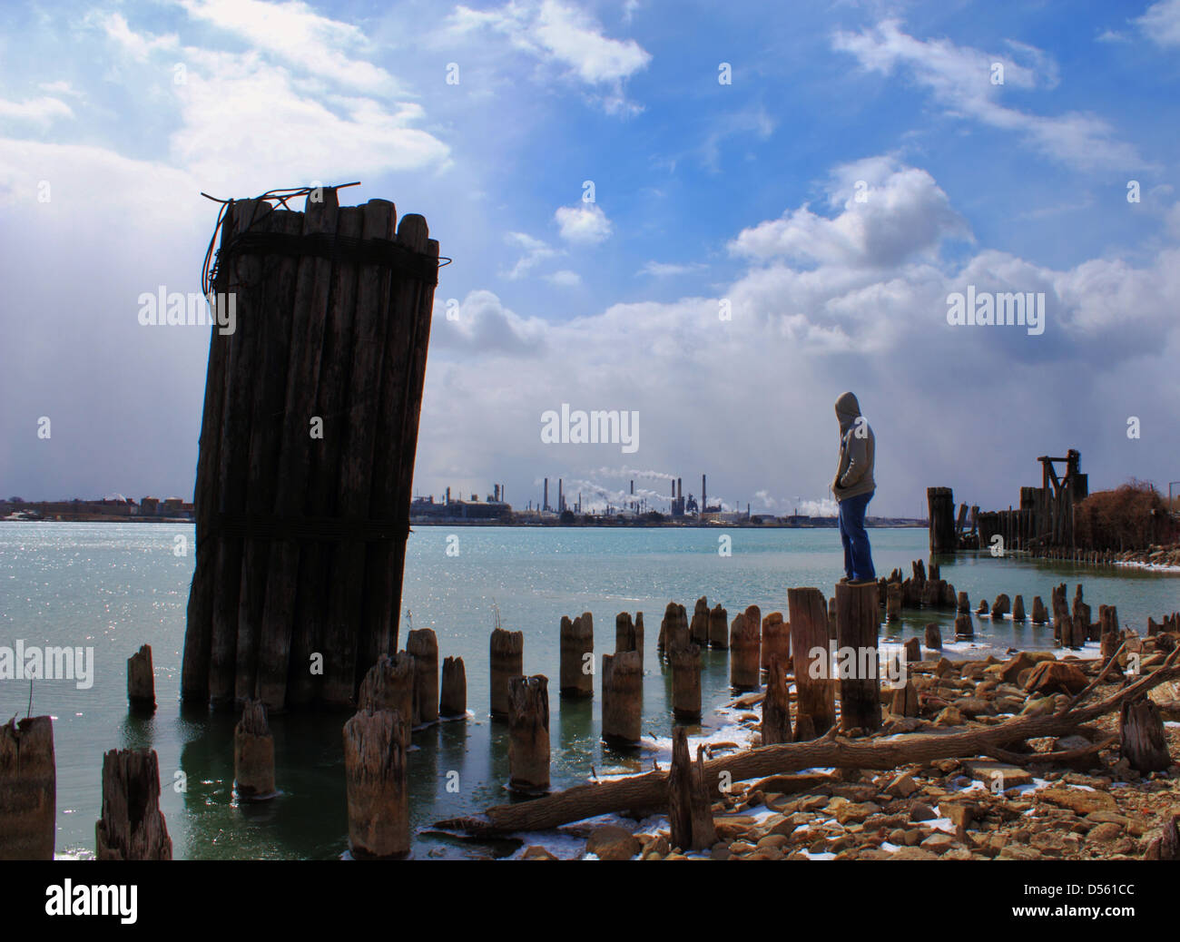 Teenager with factories and smokestacks in the background. Evidence of water pollution in the foreground. Stock Photo