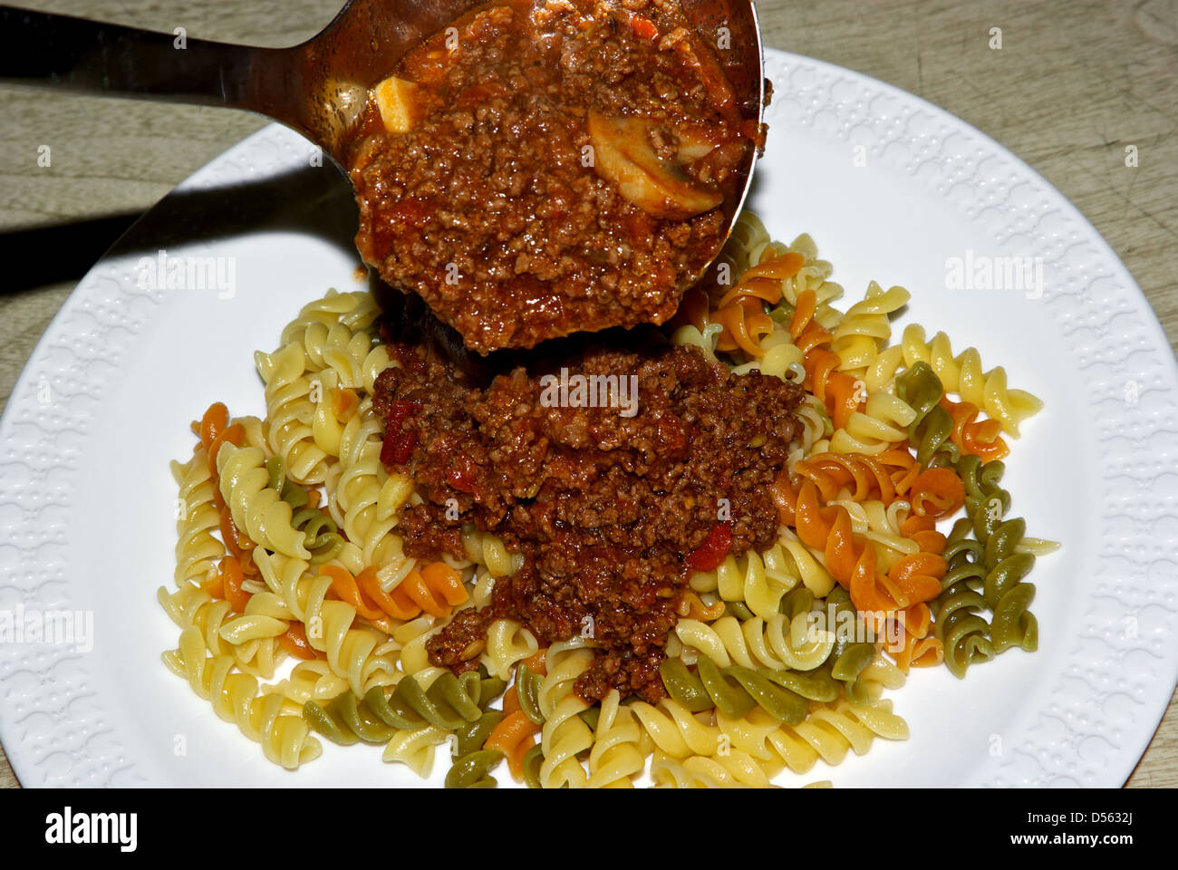 Ladle rich tomato mushroom meat Bolognese sauce over plate steaming hot cooked tricolour rotini pasta Stock Photo