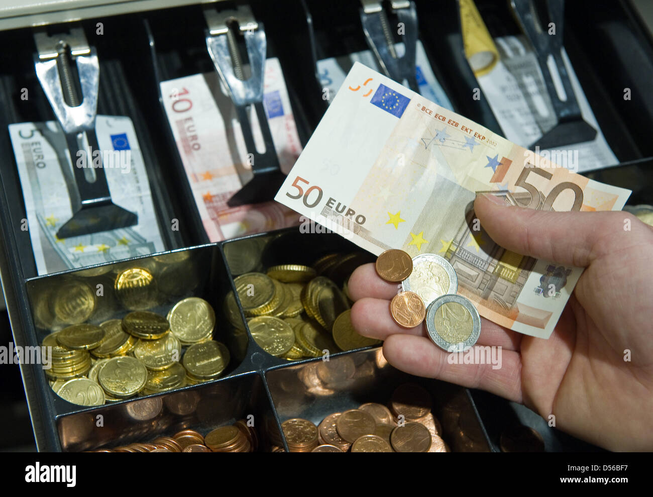 A hand holds money against the background of a full cash register in