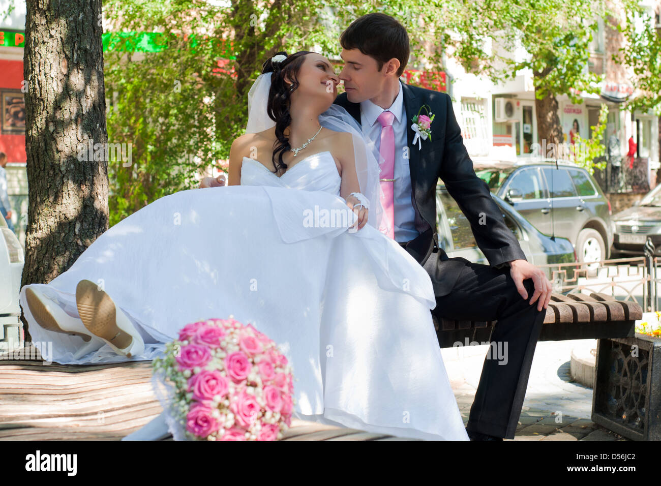 beautiful groom and the bride sit on a bench in park among green ...