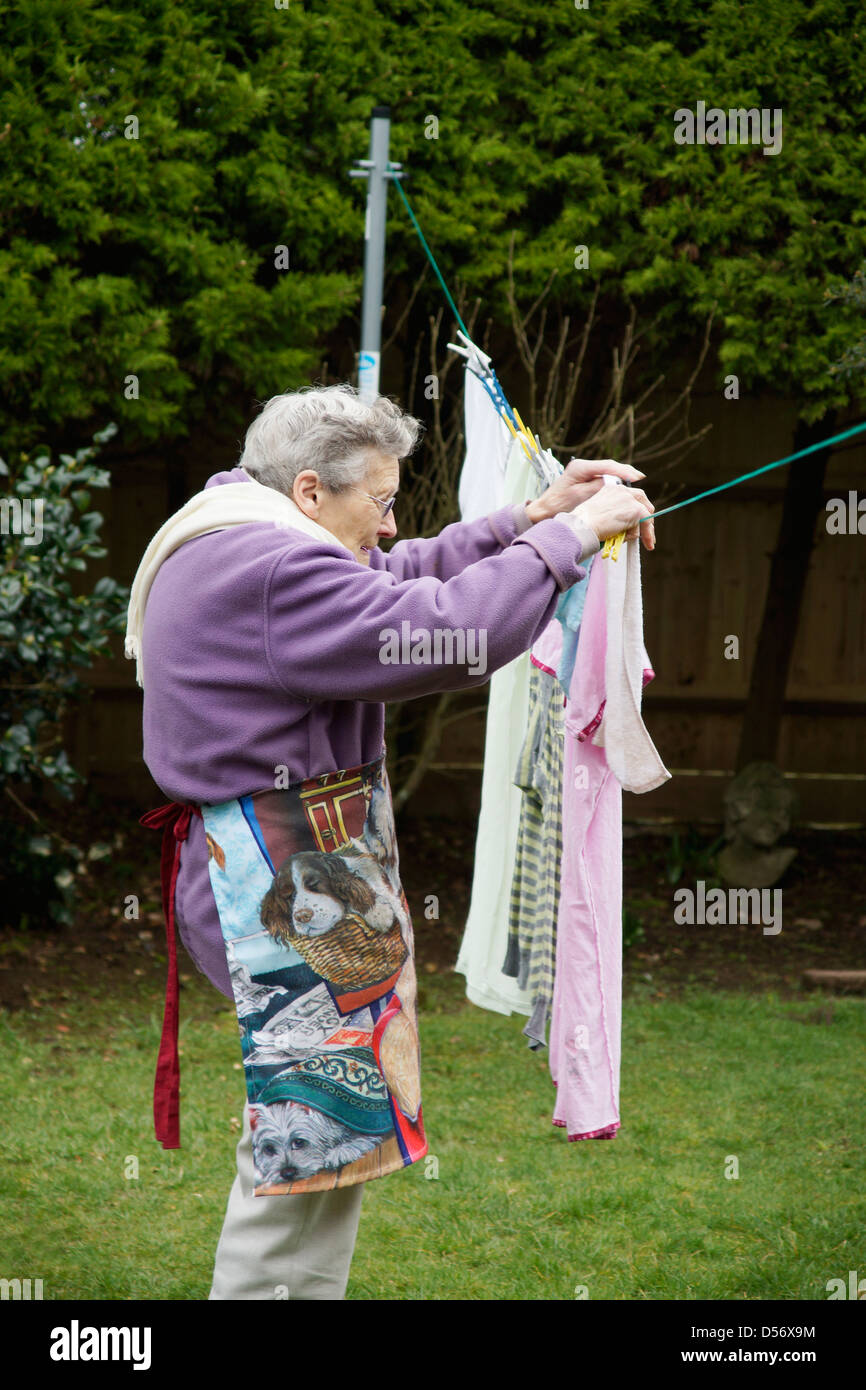 Elderly woman hanging out washed clothes for natural drying in the garden on a windy day Stock Photo