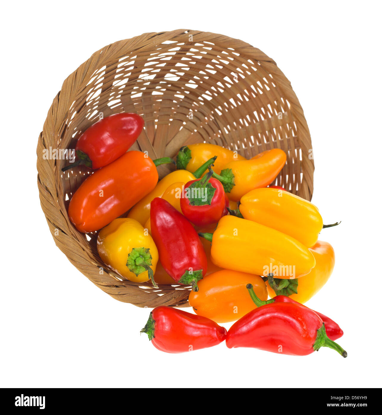 A wicker basket on it's side spilling several small sweet peppers onto ...