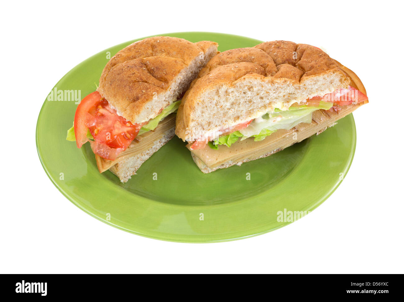 A wheat bulky roll tofu meatless turkey sandwich with lettuce tomatoes and mayonnaise sliced in half on a green plate. Stock Photo
