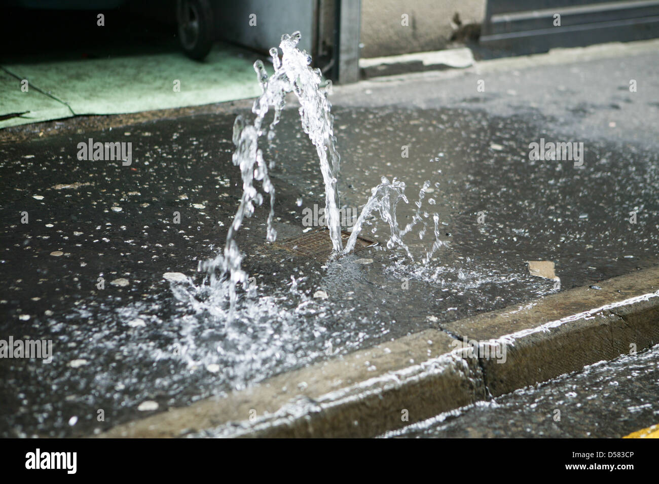 A Stopcock on the Pavement has failed causing a small fountain of water to run off Stock Photo