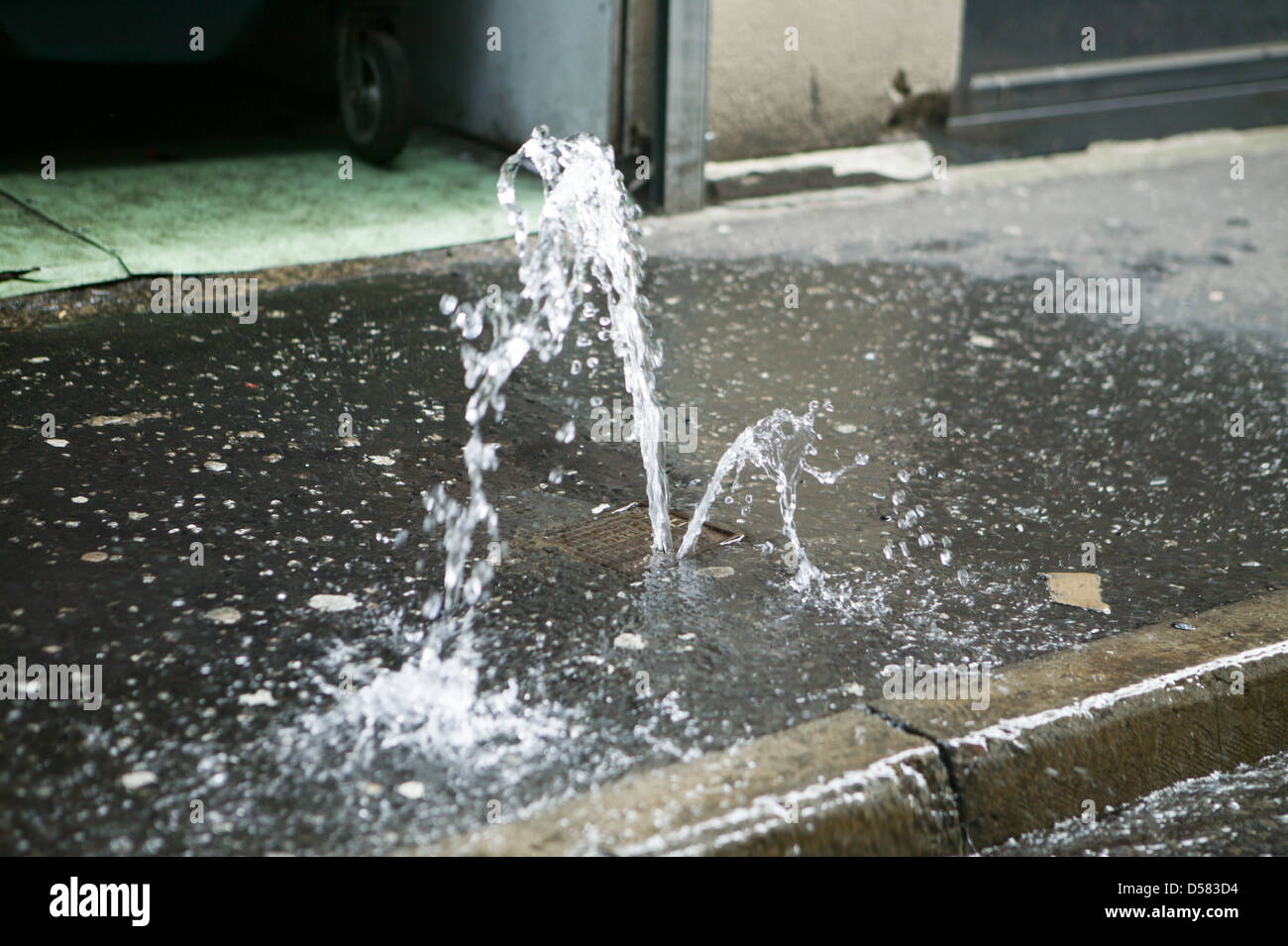 A Stopcock on the Pavement has failed causing a small fountain of water to run off Stock Photo