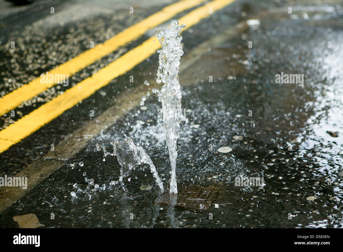 A Stopcock on the Pavement has failed causing a small fountain of water to run off Stock Photo