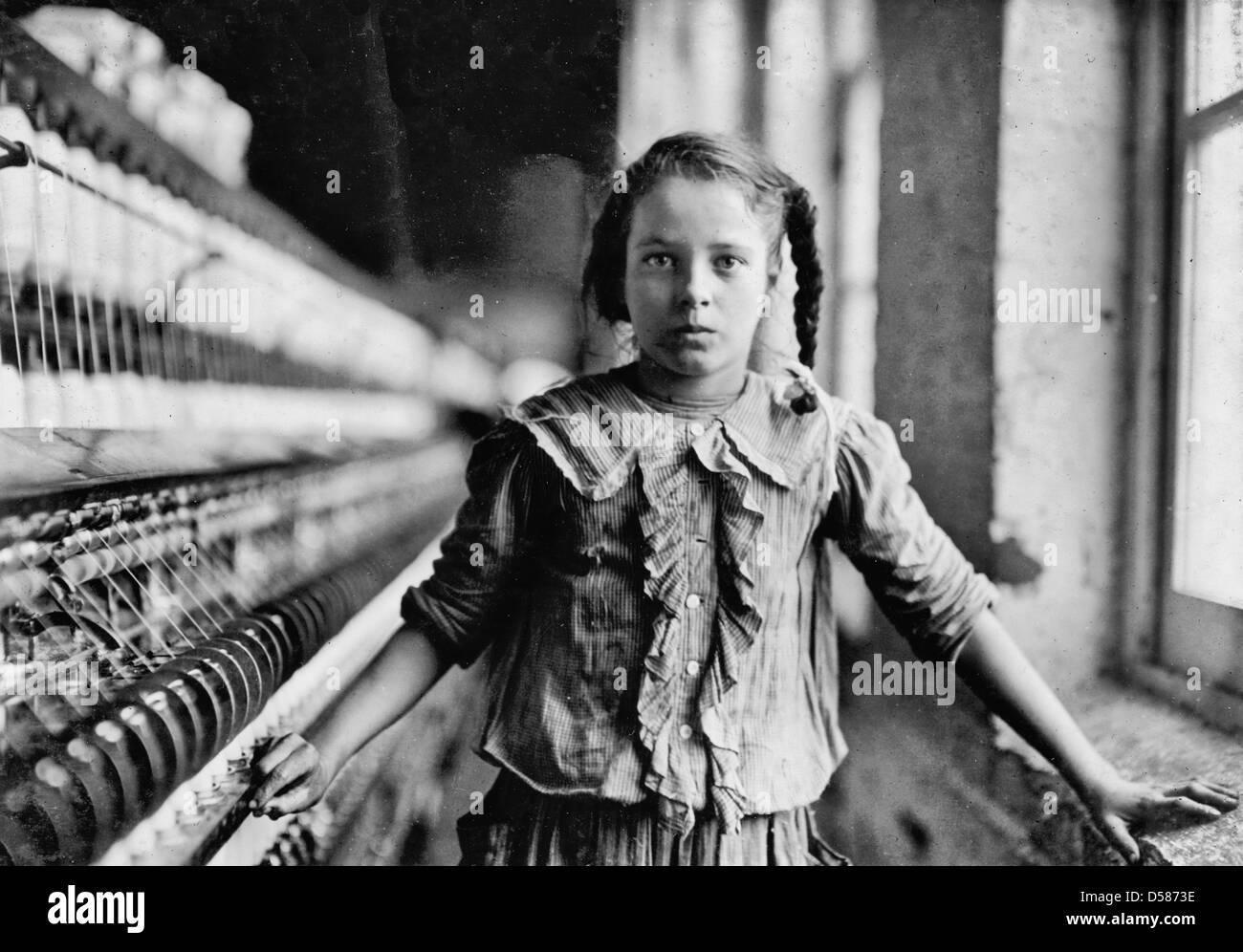 One of the spinners in Whitnel Cotton Mfg. Co. N.C. She was 51 inches high. Had been in mill 1 year. Some at night. Runs 4 sides, 48 cents a day. When asked how old, she hesitated, then said 'I don't remember.' Then confidentially, 'I'm not old enough to work, but I do just the same.' Out of 50 employees, ten children about her size. . Location: Whitnel, North Carolina. Circa 1908 Stock Photo