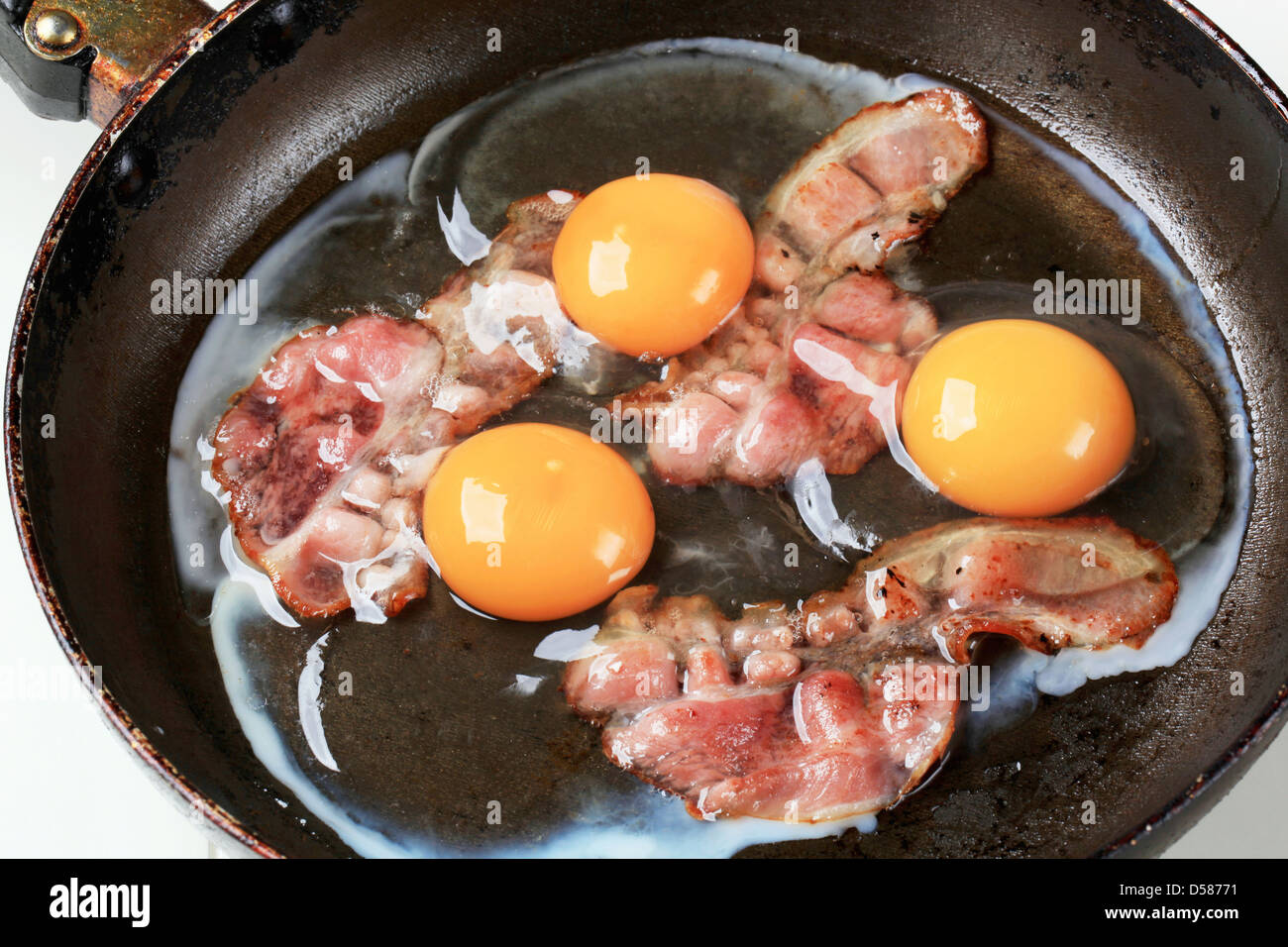 Preparing fried eggs with strips of bacon Stock Photo