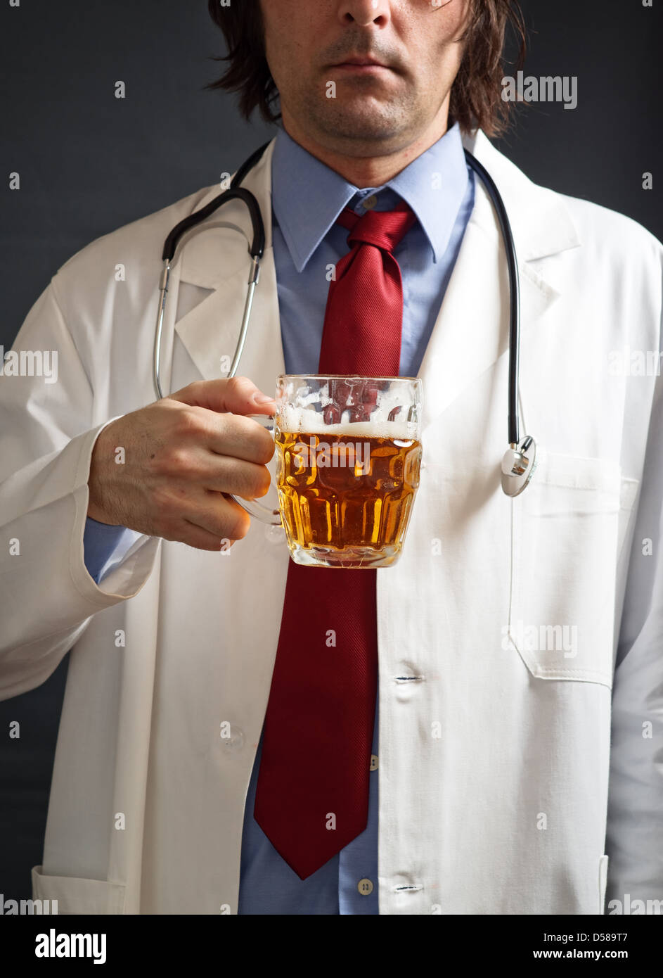 Male doctor is drinking light beer from the glass jug. One glass of beer a day concept. Stock Photo
