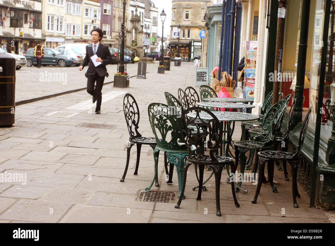 Young businessman running with a message past an empty set of street cafe tables, in Wells, Somerset, March 2013 - motion blur Stock Photo