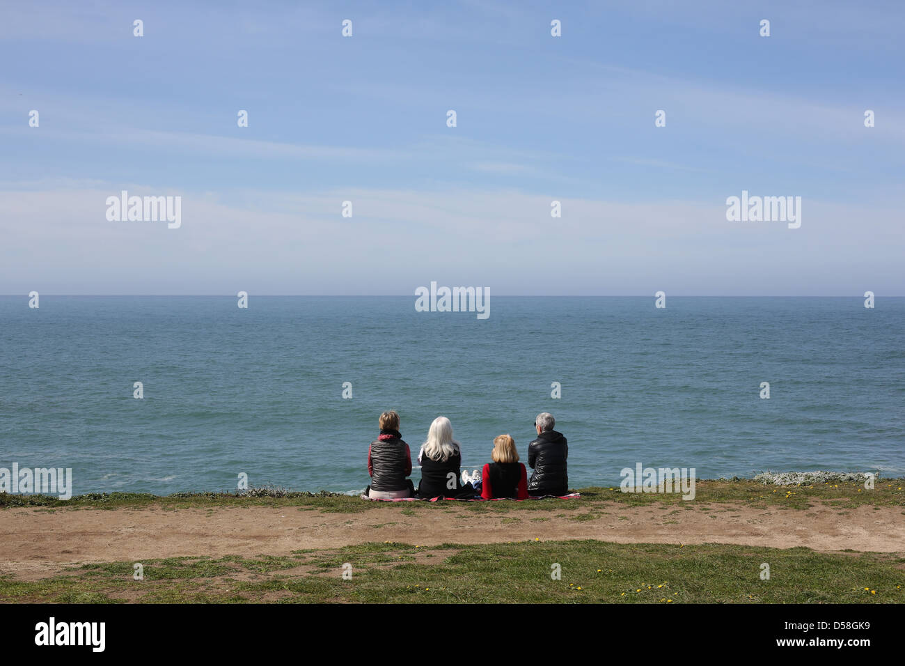 Four senior women sitting on a cliff overlooking the ocean. Stock Photo