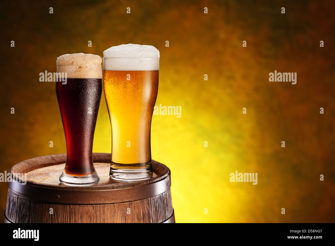 Two glasses of beer on a wooden barrel. Dark yellow background with a gradient. Stock Photo
