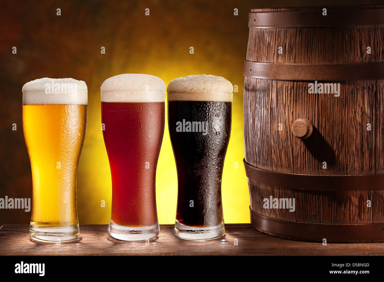 Three beer glasses with a wooden barrel. Background - dark yellow gradient. Stock Photo