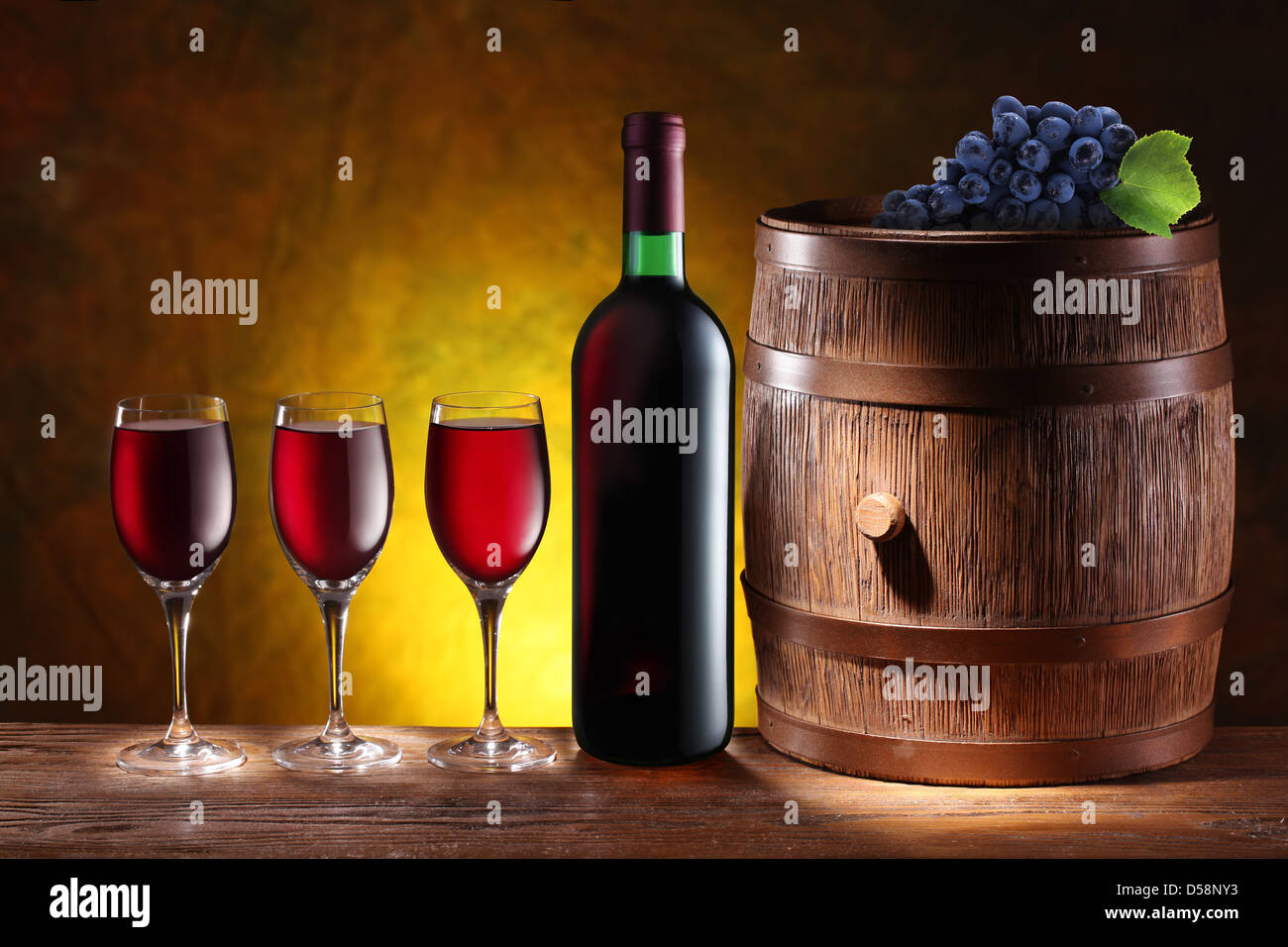 Bottle and a glass of wine with a wooden barrel on dark yellow background with a gradient. Stock Photo