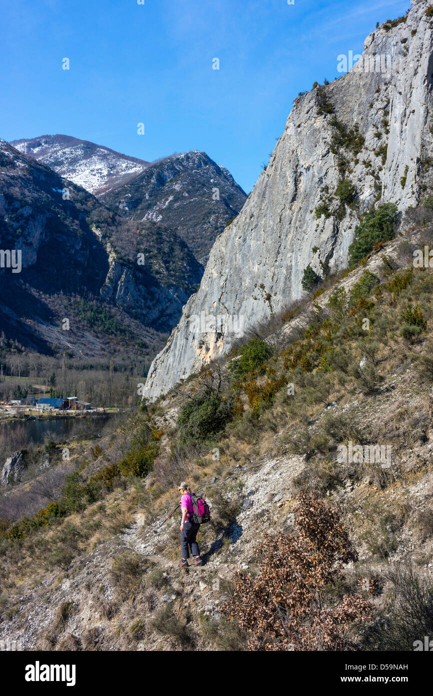 Female walker approaches cliff, snowy mountains Stock Photo