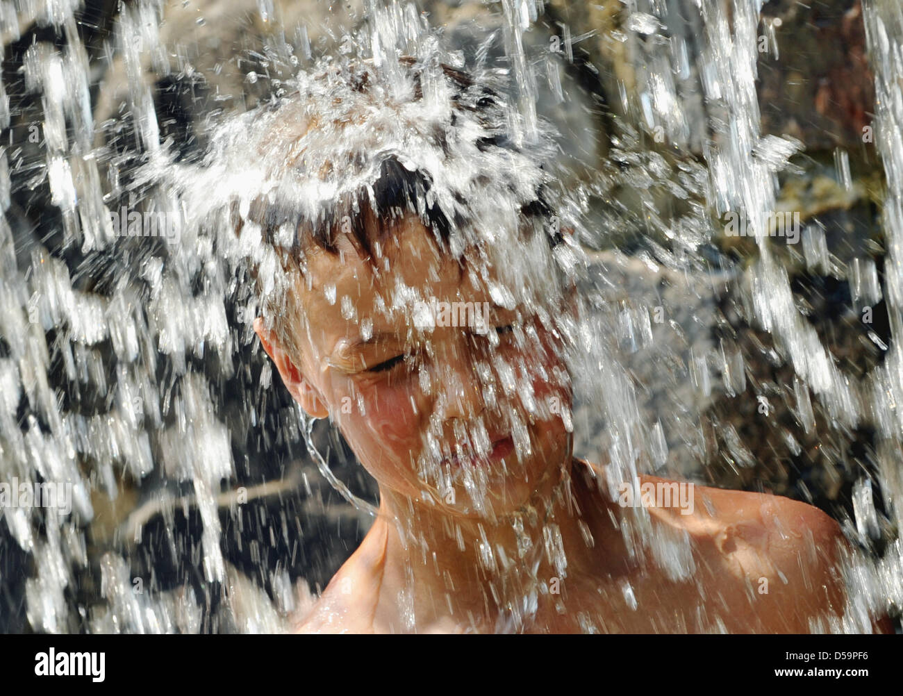 Ten-year-old Cedrik from Marburg is cooling off under a waterfall at the Edersee barrier wall near Edertal, Germany, 29 June 2010. The summer's first heat wave rolls over Hesse. In certain parts, temperatures are expected to reach 35 degrees. There is a risk of lightnung summer storms. Photo: Uwe Zucchi Stock Photo