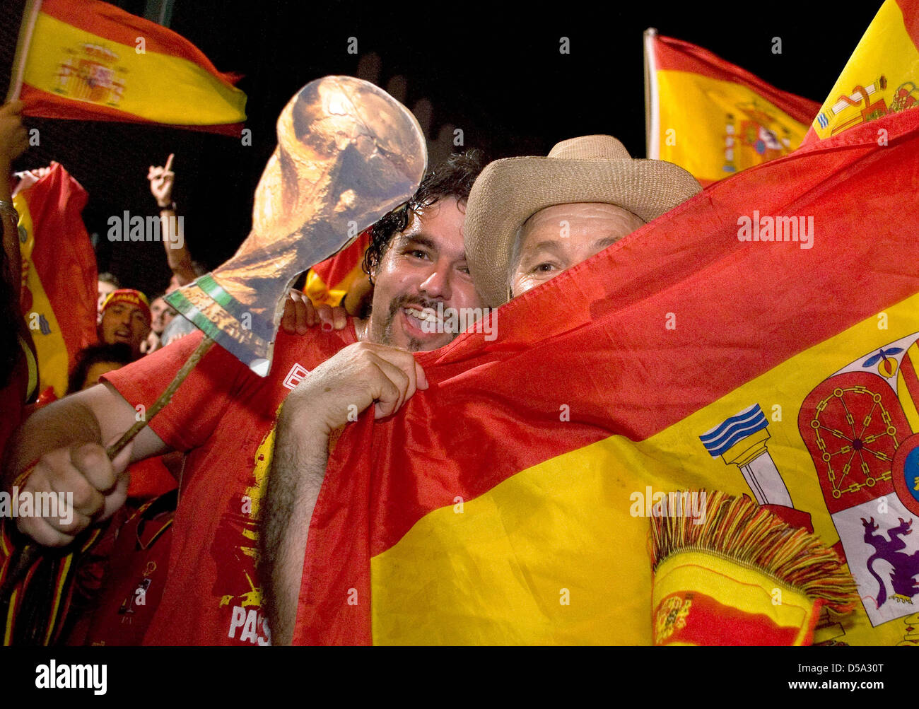 With flags and a cardboard World Cup, Spanish fans celebrate the victory of their team of the final match Spain vs. the Netherlands of the 19th FIFA World Cup 2010 on the streets of Hannover, Germany, 11 July 2010. Spain won against the Netherlands 1-0 and is World Champion for the first time. Photo: Michael Löwa Stock Photo