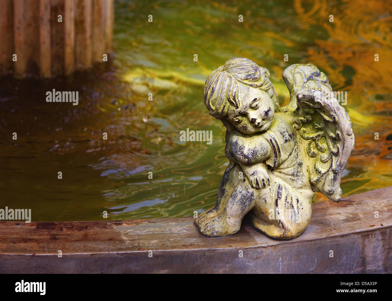 Cherub next to the fountain. Statue of cute little angel made of stone. Beautiful warm colors
