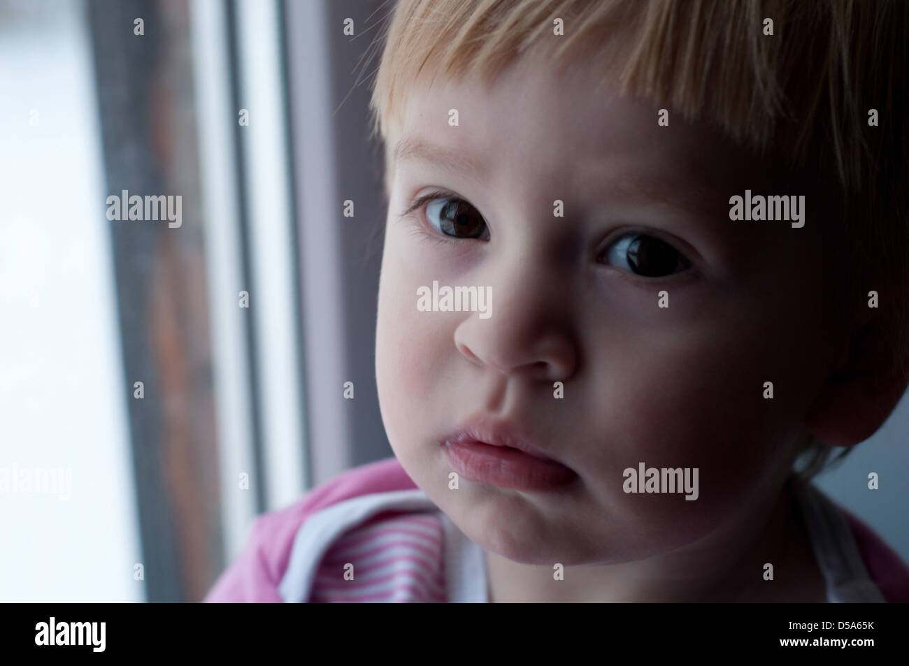 the small baby is standing near white wall and thoughtful looking long way off Stock Photo