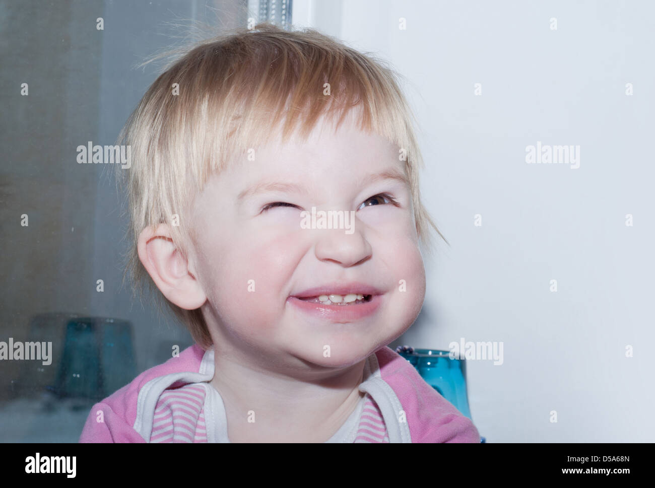 the small baby is standing near white wall and nice grimace Stock Photo