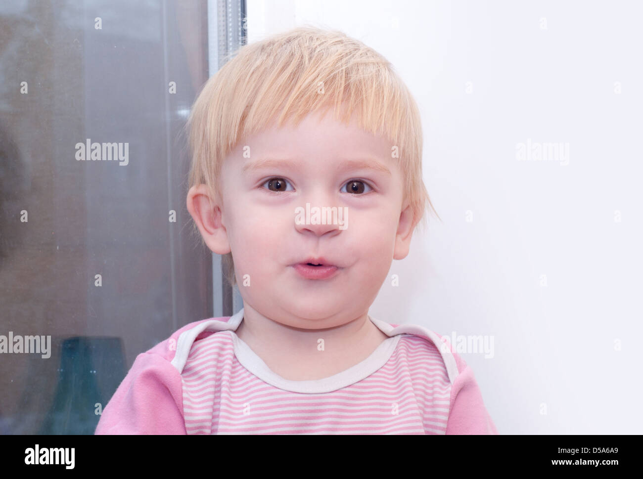 the small baby is standing near white wall and nice grimace Stock Photo