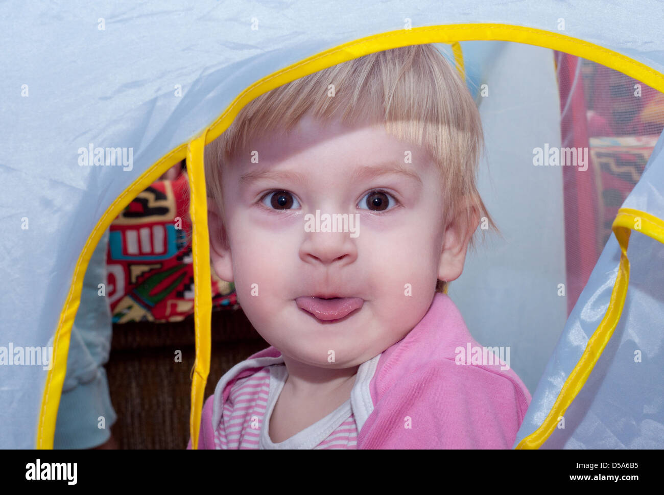 the nice child is siting in the blue baby's house and showing tongue Stock Photo