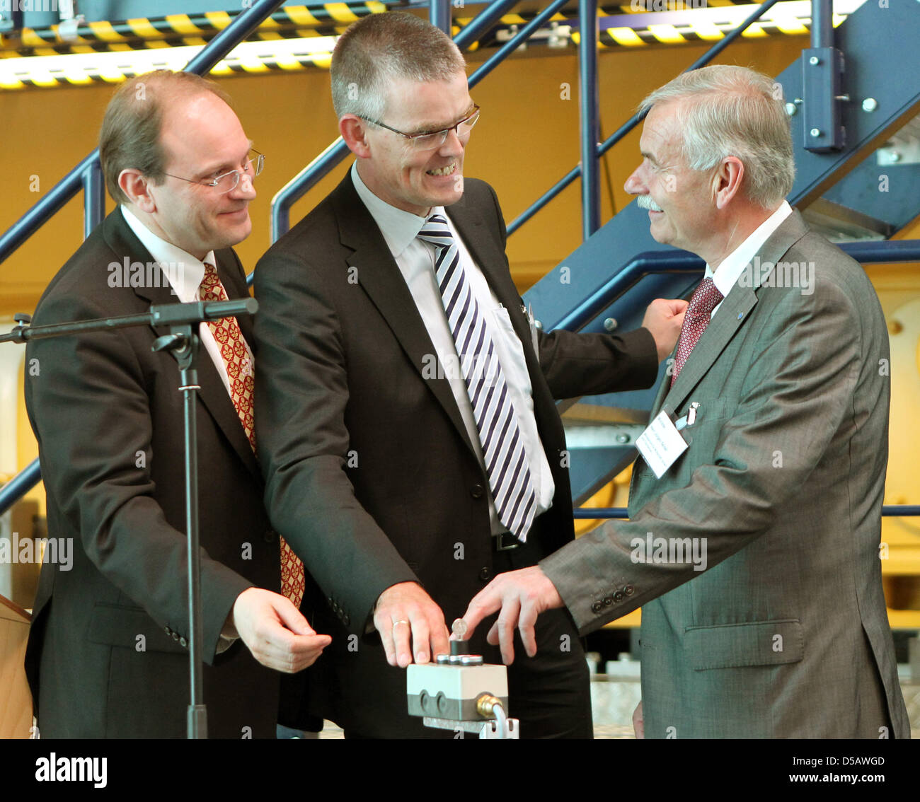 Economic Minister of Mecklenburg West-Pomerania, Juergen Seidel (R), presses a button that starts a diesel engine in a test bed in Rostock, Germany, 26 June 2010. Accompanying him are Dirk Jebsen (C), production manager of Caterpillar Kiel and Rostock, and Richard Case (L), Vice President of Caterpillar Marine and Petroleum Power Division. Caterpillar Motors Rostock celebrates its  Stock Photo