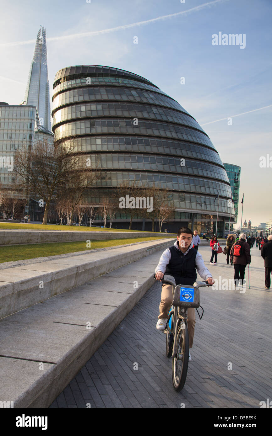 A man riding a 'Boris bike' outside City Hall on the south bank of the Thames in London. Stock Photo