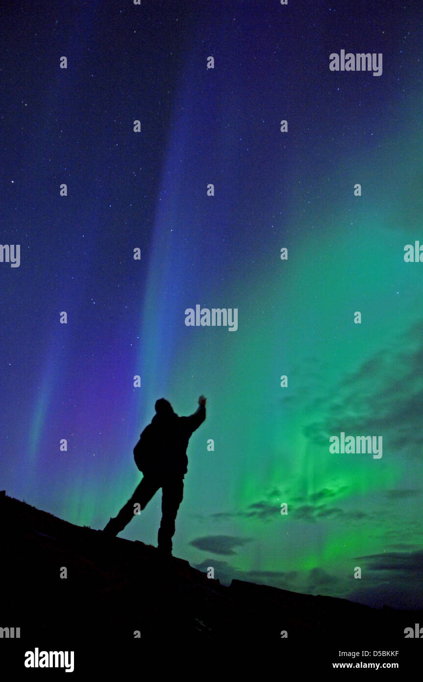 A man looks at the night sky with polar lights over the Finnmark nearby Repvag, Norway, 5 September 2010. These northern lights are caused by giant clouds of electrically charged particles of a sunstorm that hit the atmosphere. The polar light result when the atoms of the upper atmosphere above 100 km, are stimulated by corpuscular radiation from the sun, and start to glow. Polar l Stock Photo