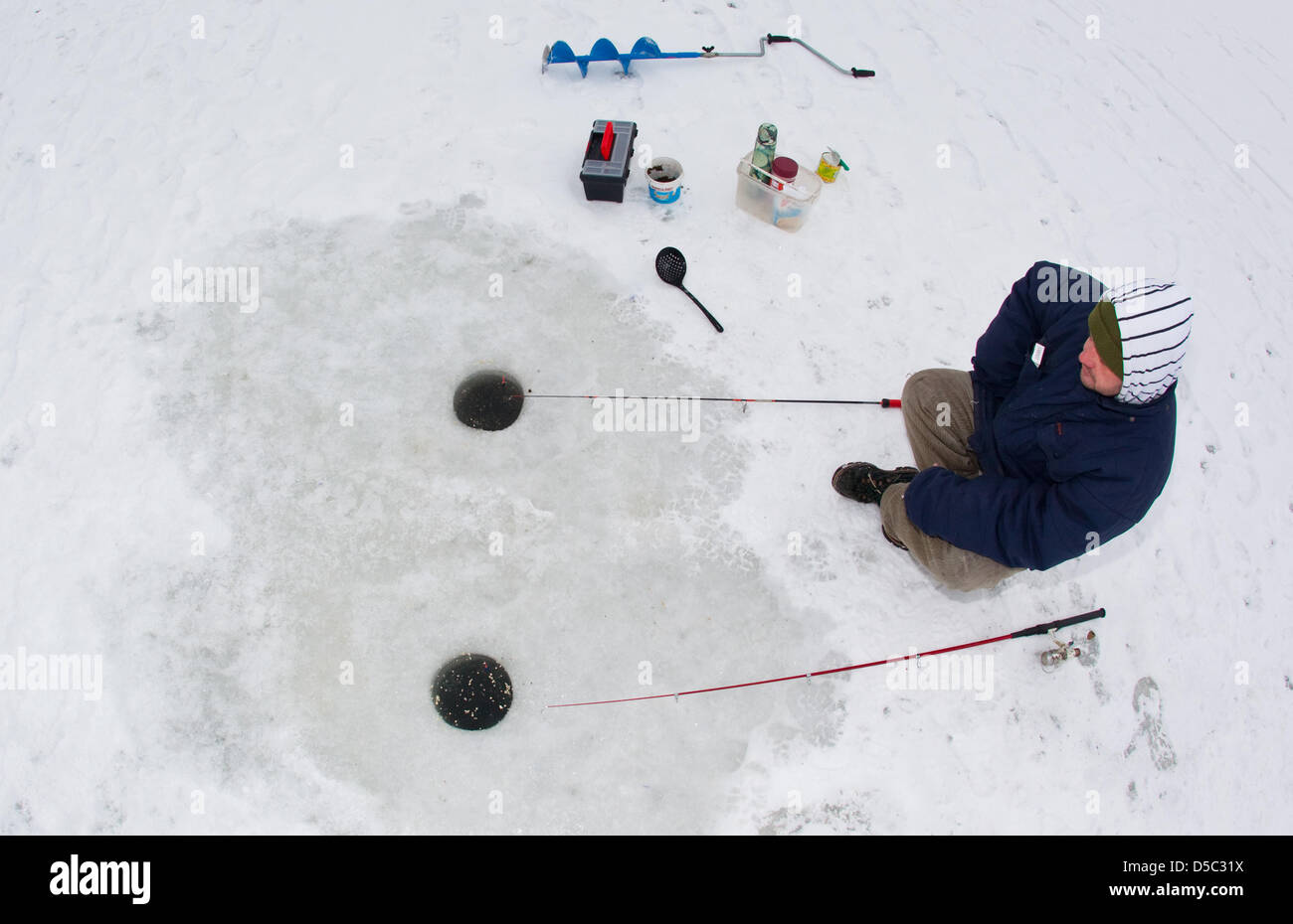 Ice fisher Danny Frohbert waits for a catch next to holes in the 25-centimetre-thick ice on the frozen over Oder-Spree-canal in Muellrose, Germany, 27 January 2010. Photo: Patrick Pleul Stock Photo