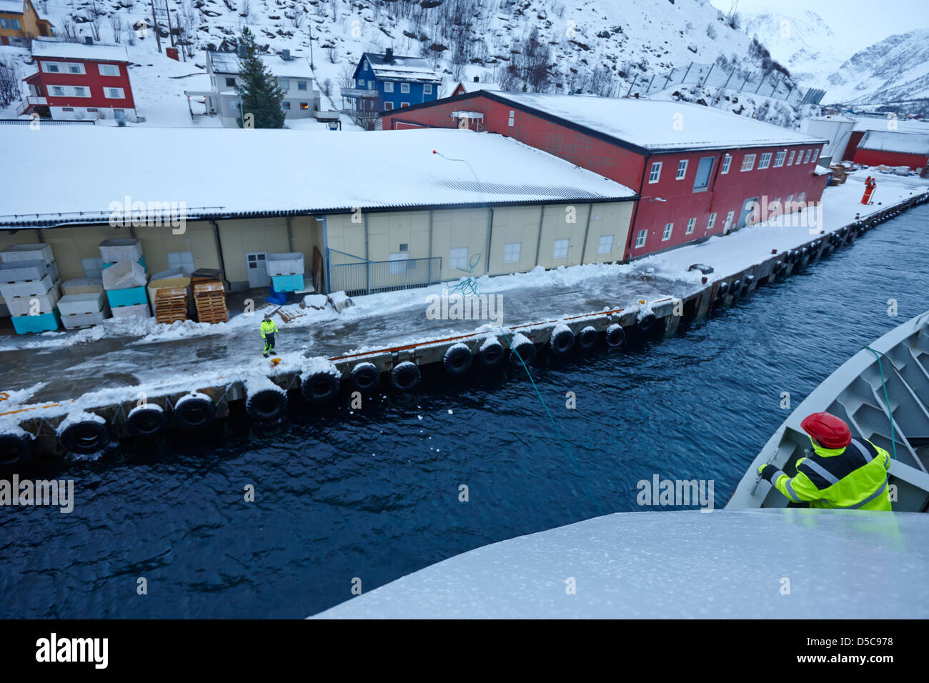 hurtigruten crew member throws ships rope guide line to dock worker oksfjord during winter norway europe Stock Photo