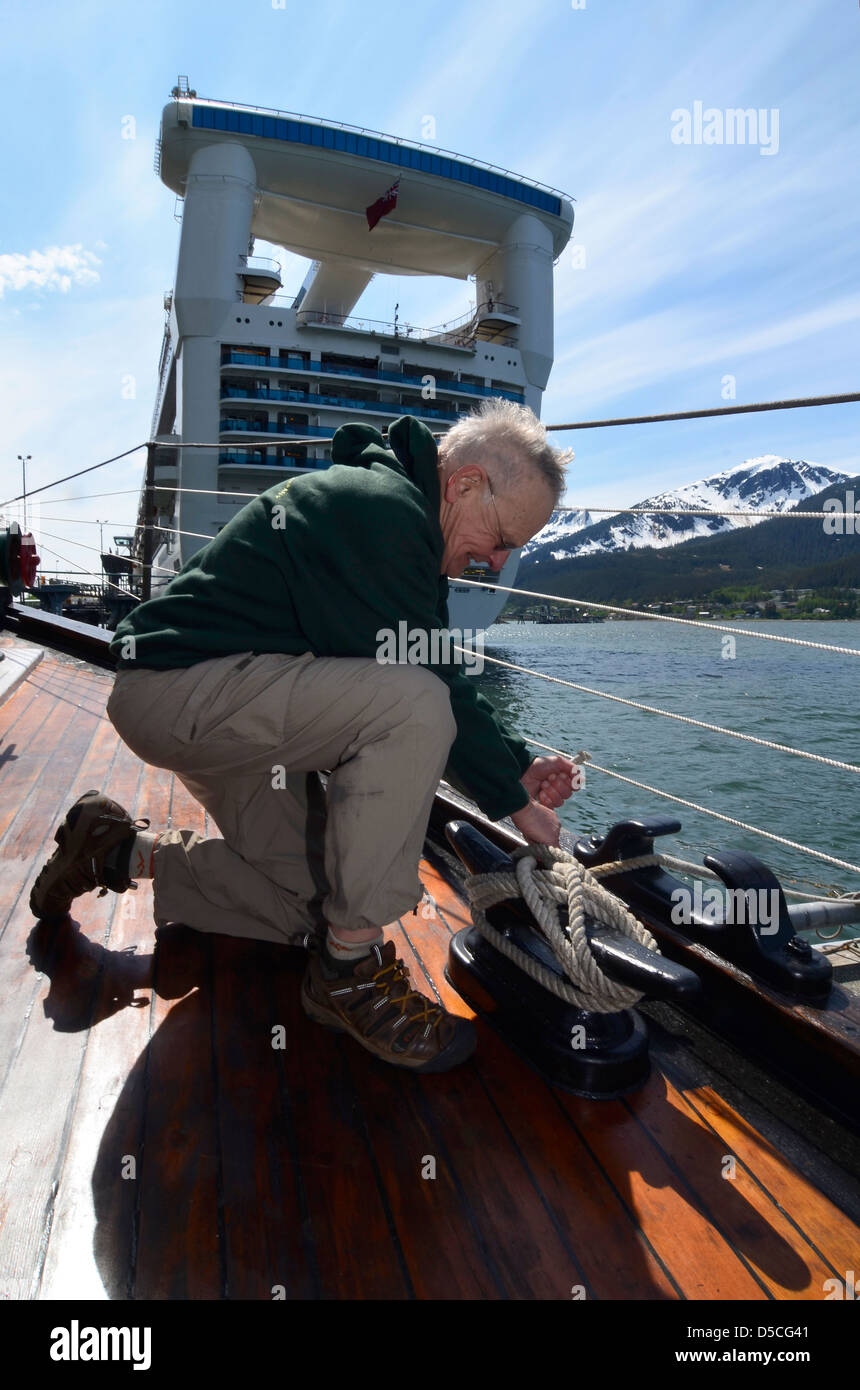Tying a rope to a cleat on a small tour boat while docking near a large cruise ship in Juneau, Alaska. Stock Photo