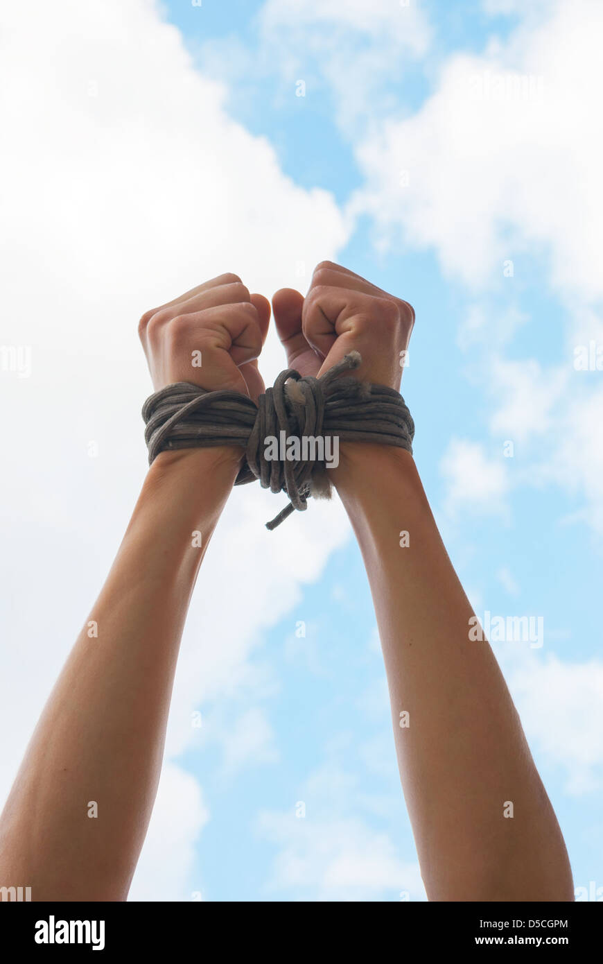 Hands tied up with rope against blue sky Stock Photo