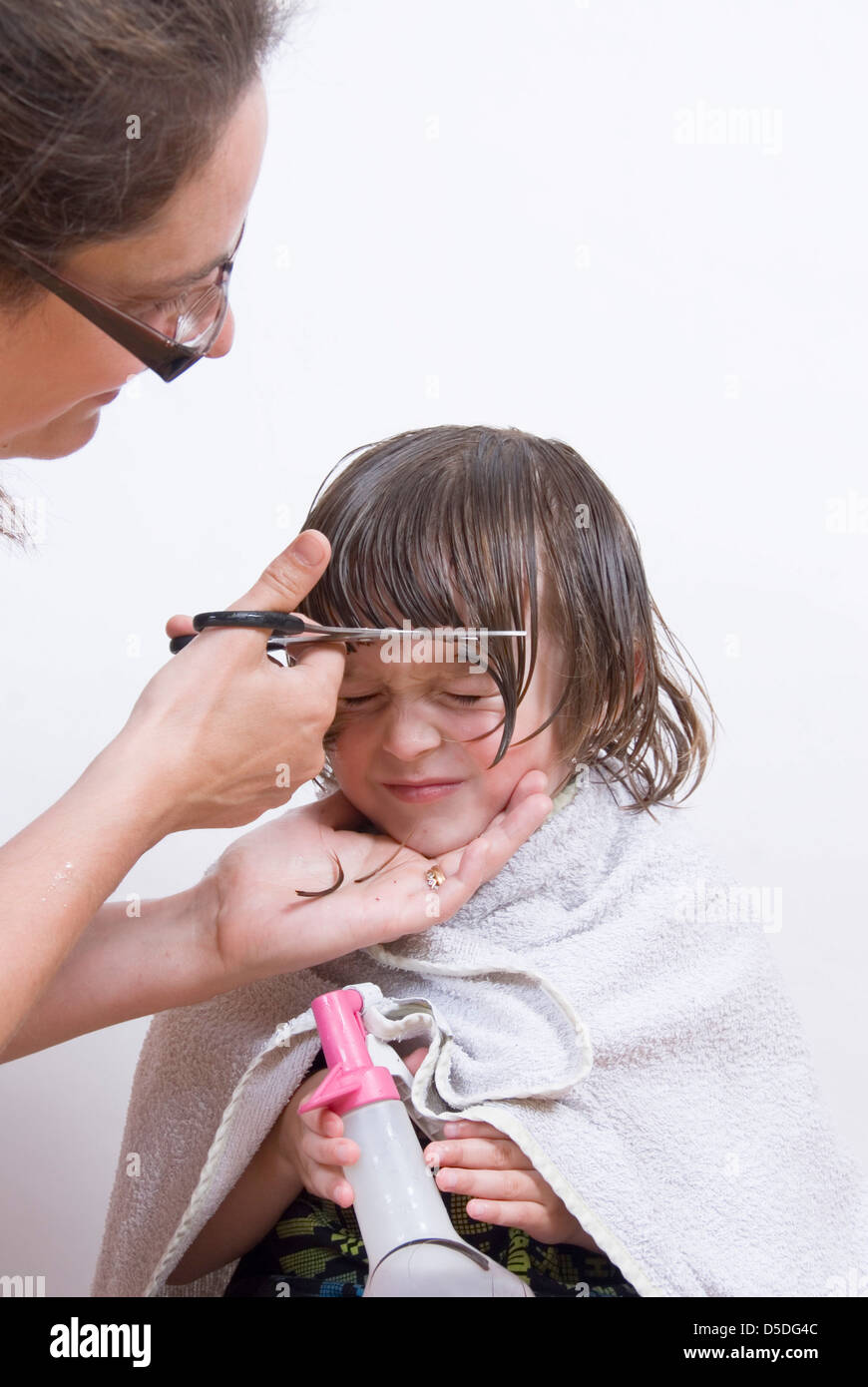 Young boy scrunches face as scissors cut his fringe mother cutting