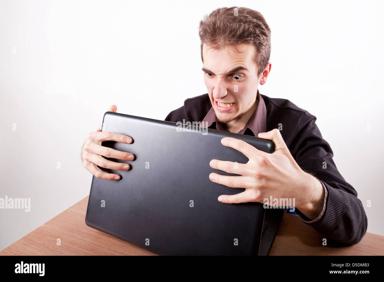 young man holding a laptop with both hands on a desk very angry and upset Stock Photo
