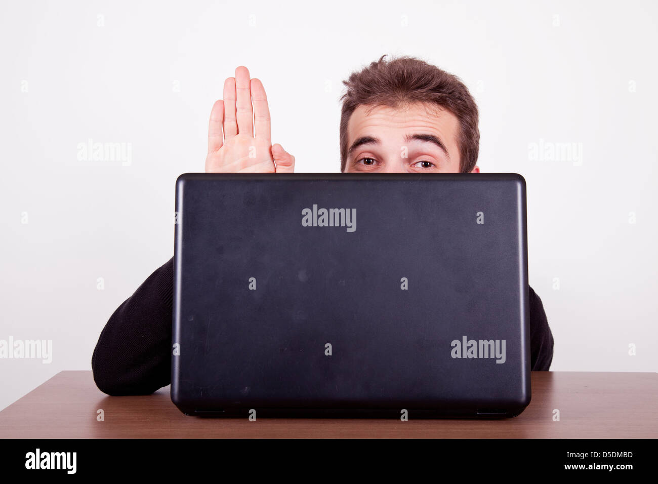 shy young man waving hello from behind a laptop screen Stock Photo